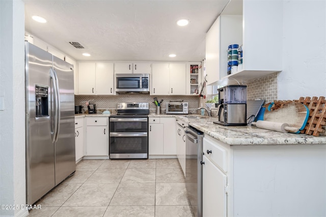 1052 Tompkins Dr, Port Orange, FL 32129 - kitchen with stainless steel appliances, decorative backsplash, white cabinetry, recessed lighting, and light stone countertops
