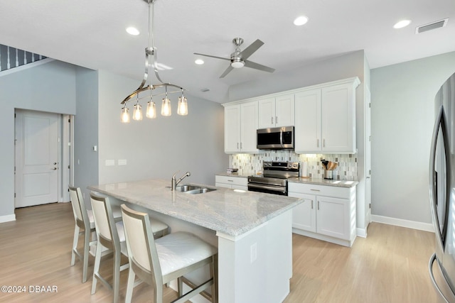 kitchen with light stone countertops, white cabinetry, stainless steel appliances, an island with sink, and decorative light fixtures