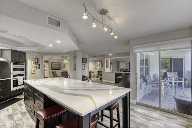 1 John Anderson Dr Unit 103, Ormond Beach, FL 32176 - kitchen with white double oven, a kitchen breakfast bar, light stone countertops, and light wood-style flooring