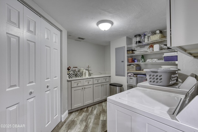 1 John Anderson Dr Unit 103, Ormond Beach, FL 32176 - washroom featuring washing machine and clothes dryer, electric panel, light wood finished floors, cabinet space, and a textured ceiling