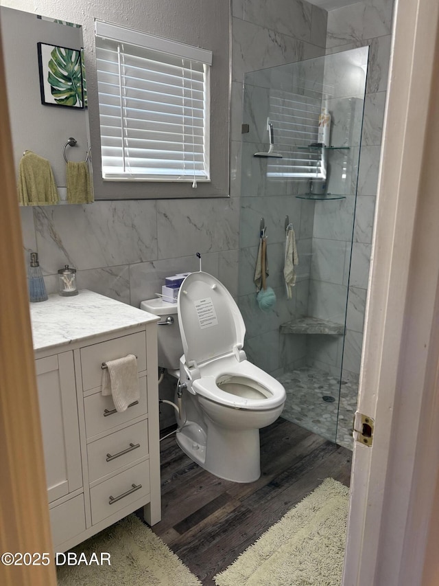 bathroom featuring tile walls, hardwood / wood-style flooring, vanity, tiled shower, and toilet