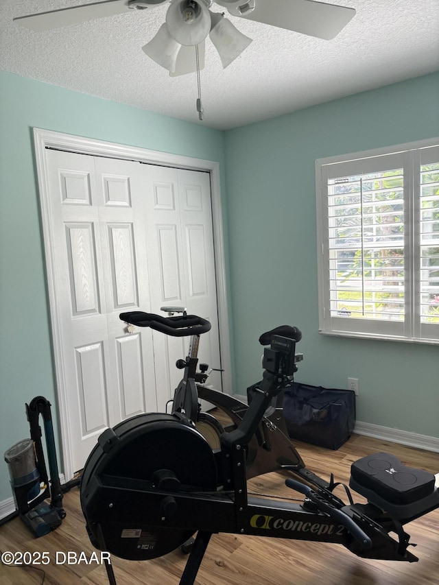 exercise room featuring ceiling fan, wood-type flooring, and a textured ceiling