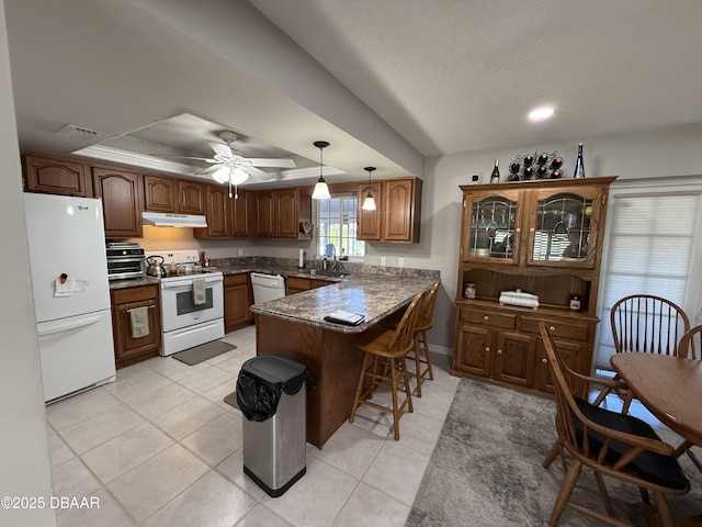 kitchen featuring a tray ceiling, decorative light fixtures, a kitchen bar, kitchen peninsula, and white appliances