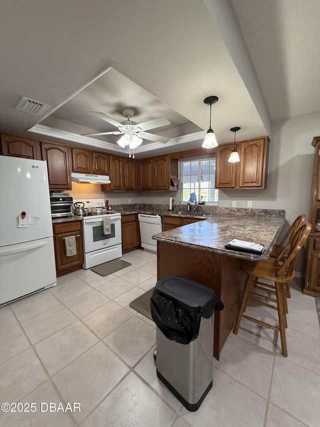 kitchen featuring a tray ceiling, a kitchen breakfast bar, hanging light fixtures, kitchen peninsula, and white appliances