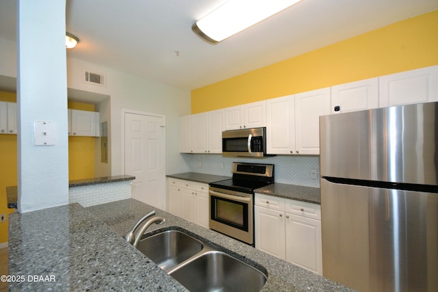 kitchen featuring appliances with stainless steel finishes, dark stone counters, and white cabinets