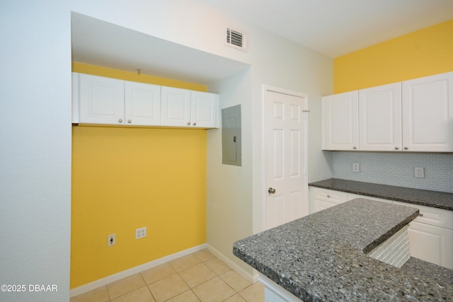 kitchen featuring white cabinetry, backsplash, dark stone countertops, electric panel, and light tile patterned flooring