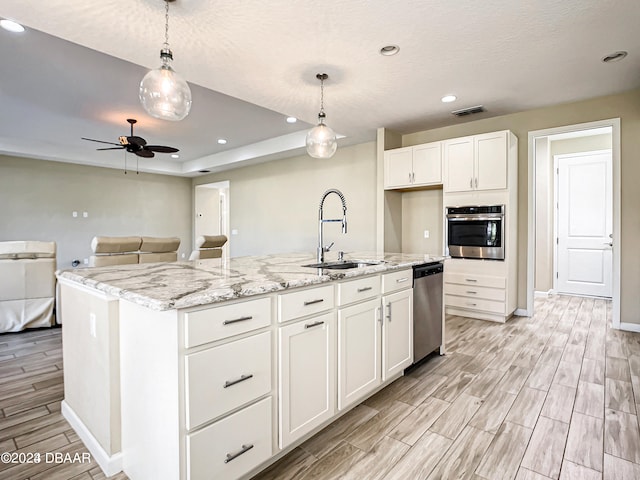 kitchen featuring stainless steel appliances, decorative light fixtures, sink, white cabinets, and a kitchen island with sink