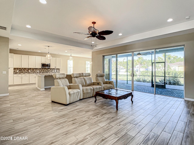 living room featuring light hardwood / wood-style floors, ceiling fan, and a tray ceiling