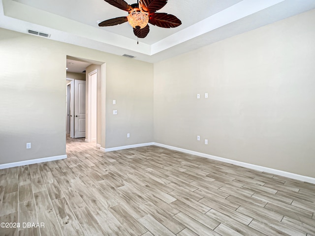 empty room featuring ceiling fan, light wood-type flooring, and a tray ceiling