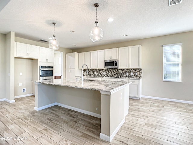 kitchen with a kitchen island with sink, appliances with stainless steel finishes, sink, and pendant lighting