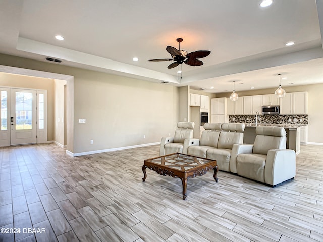 living room with french doors, sink, ceiling fan, a raised ceiling, and light wood-type flooring