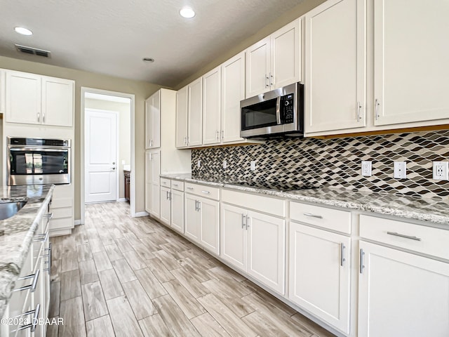 kitchen with light hardwood / wood-style floors, white cabinets, tasteful backsplash, light stone countertops, and appliances with stainless steel finishes