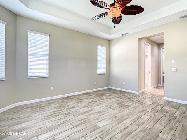 unfurnished room with light wood-type flooring, ceiling fan, and a raised ceiling