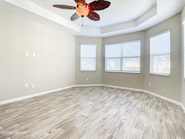 empty room with light hardwood / wood-style floors, ceiling fan, and a raised ceiling