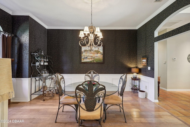 dining area with wood-type flooring, ornamental molding, and a notable chandelier