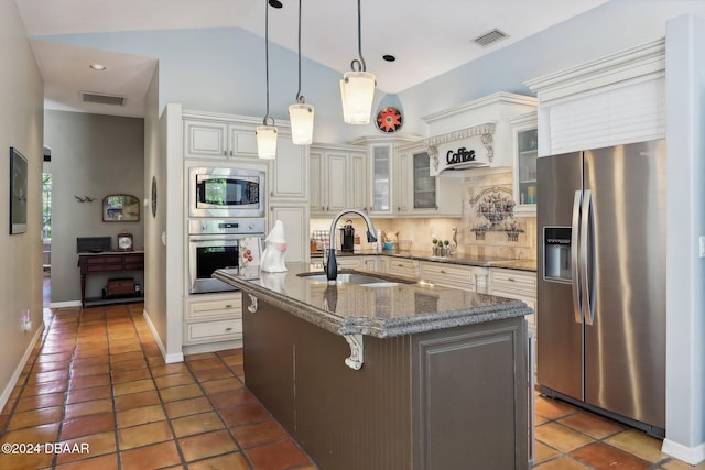 kitchen featuring dark stone counters, a center island with sink, sink, tasteful backsplash, and stainless steel appliances