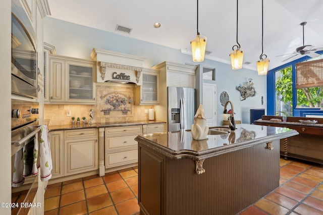 kitchen with decorative backsplash, cream cabinets, stainless steel appliances, and a center island with sink