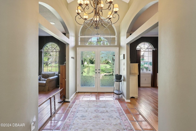 doorway to outside featuring an inviting chandelier, wood-type flooring, a towering ceiling, and french doors