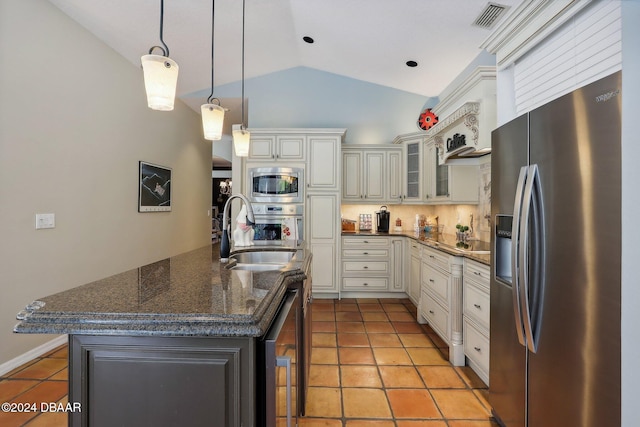 kitchen featuring stainless steel appliances, vaulted ceiling, sink, a center island with sink, and dark stone countertops