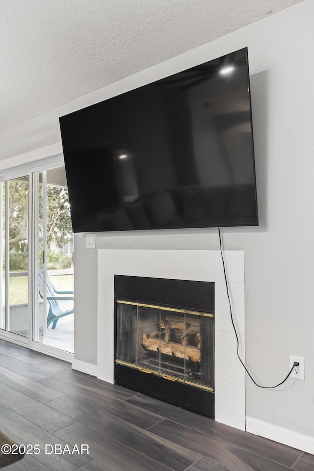 room details featuring a textured ceiling, a fireplace, baseboards, and wood finished floors