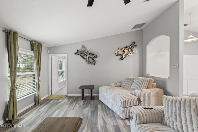 living room with wood finished floors, a ceiling fan, visible vents, vaulted ceiling, and baseboards