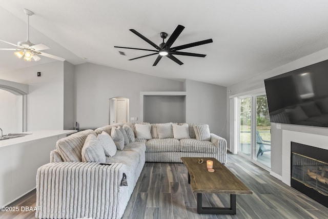 living room with lofted ceiling, dark wood-type flooring, visible vents, a ceiling fan, and a glass covered fireplace