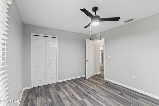 unfurnished bedroom featuring dark wood-type flooring, a closet, visible vents, and baseboards