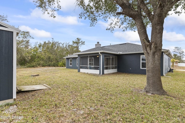 back of property featuring a sunroom, a chimney, a lawn, and roof with shingles