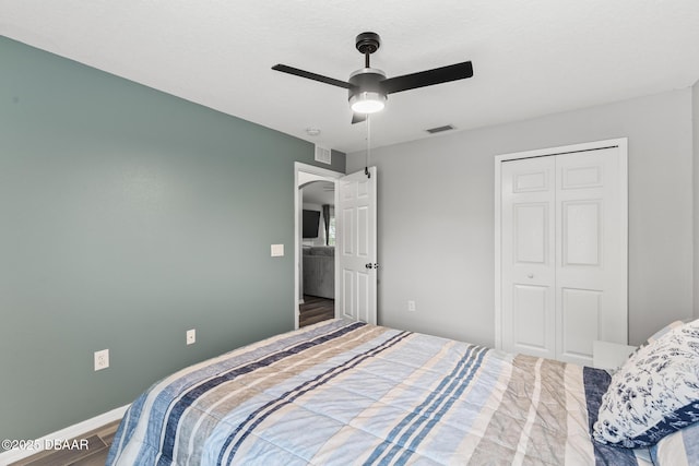 bedroom with baseboards, visible vents, a ceiling fan, wood finished floors, and a closet