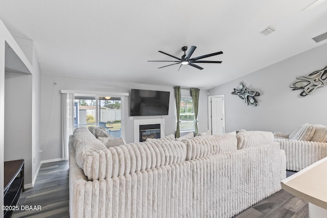 living area featuring a ceiling fan, visible vents, dark wood-type flooring, and a glass covered fireplace