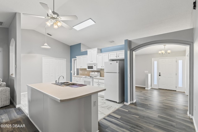 kitchen with arched walkways, white appliances, a sink, and white cabinetry