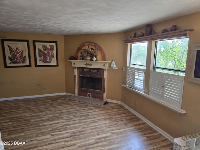 unfurnished living room featuring a fireplace with flush hearth, baseboards, wood finished floors, and a textured ceiling