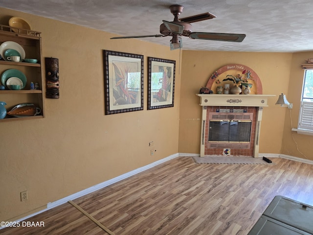 unfurnished living room with baseboards, a ceiling fan, wood finished floors, and a tiled fireplace