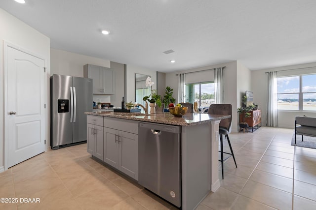 kitchen with a kitchen bar, gray cabinetry, dark stone countertops, an island with sink, and stainless steel appliances