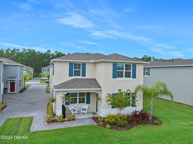 traditional-style home with a front yard, decorative driveway, roof with shingles, and stucco siding