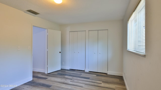 unfurnished bedroom with a textured ceiling, light hardwood / wood-style floors, and multiple closets