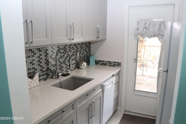 kitchen with light stone countertops, tasteful backsplash, white appliances, sink, and light tile patterned floors