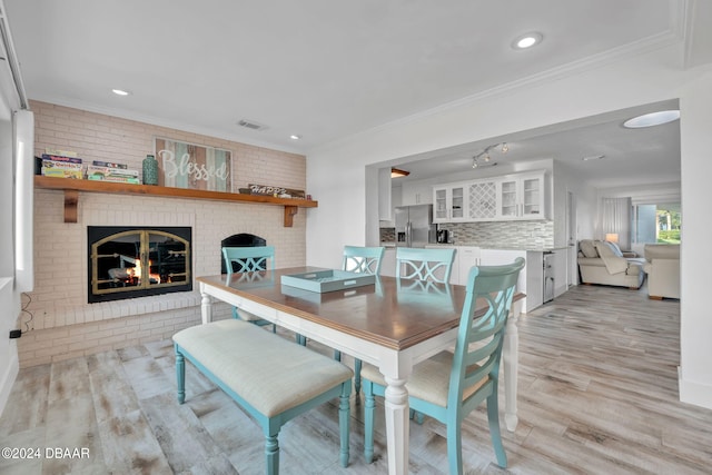 dining area with a brick fireplace, light hardwood / wood-style floors, brick wall, and crown molding