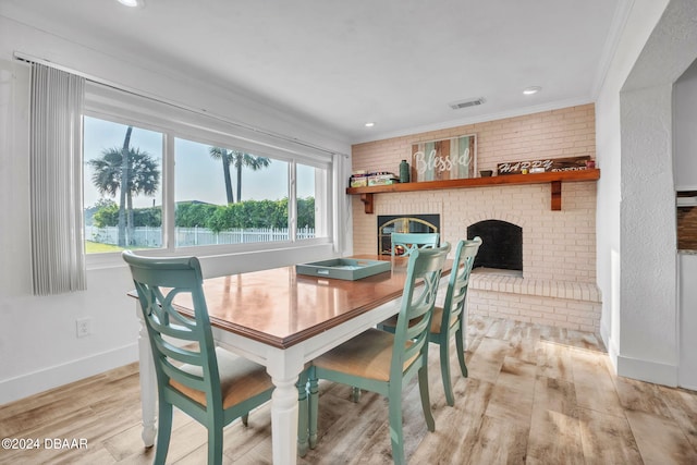 dining room featuring a brick fireplace, light hardwood / wood-style floors, brick wall, and crown molding