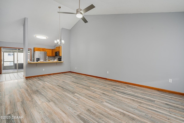 unfurnished living room with ceiling fan with notable chandelier, light wood-type flooring, and high vaulted ceiling