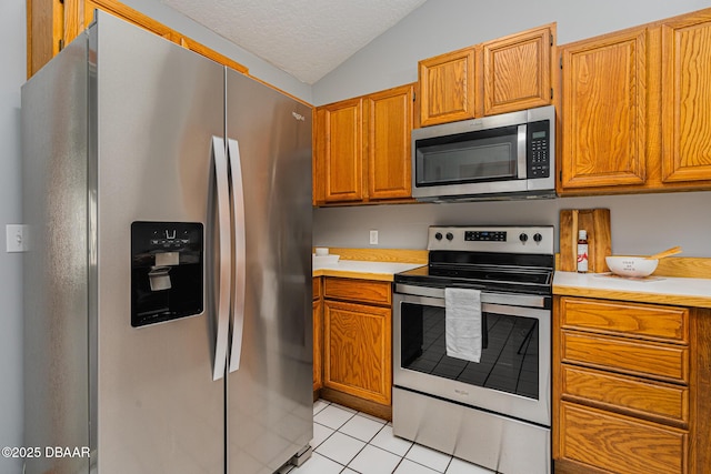 kitchen featuring a textured ceiling, light tile patterned floors, stainless steel appliances, and lofted ceiling