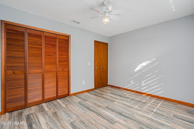 unfurnished bedroom featuring ceiling fan, a closet, light hardwood / wood-style floors, and a textured ceiling