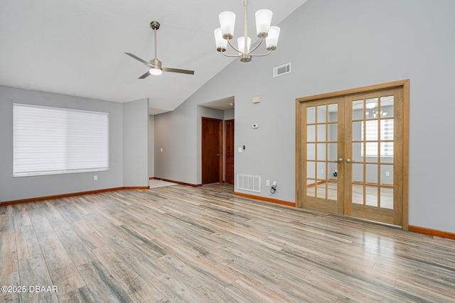 unfurnished living room with ceiling fan with notable chandelier, light hardwood / wood-style flooring, high vaulted ceiling, and french doors