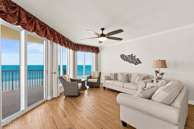 living room with a water view, ceiling fan, ornamental molding, light wood-style flooring, and a textured ceiling