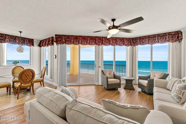 living room with a water view, a textured ceiling, ceiling fan, and hardwood / wood-style floors
