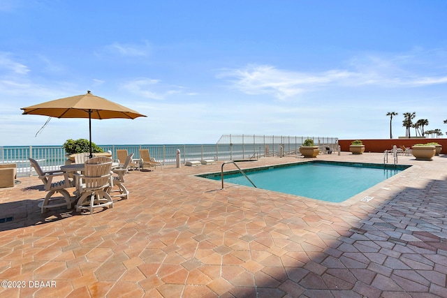 community pool with a patio area, fence, and a water view