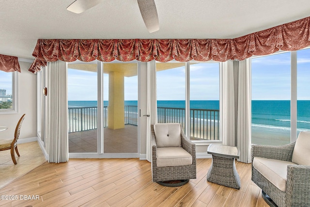 sunroom / solarium featuring view of water and beach, wood finished floors, baseboards, and a textured ceiling