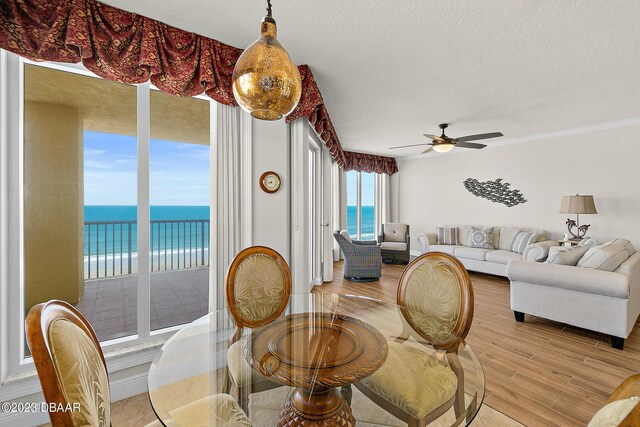 dining area with light wood finished floors, a water view, ceiling fan, crown molding, and a textured ceiling