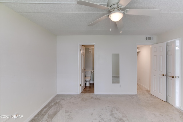 unfurnished bedroom featuring a textured ceiling, light carpet, connected bathroom, ceiling fan, and a spacious closet