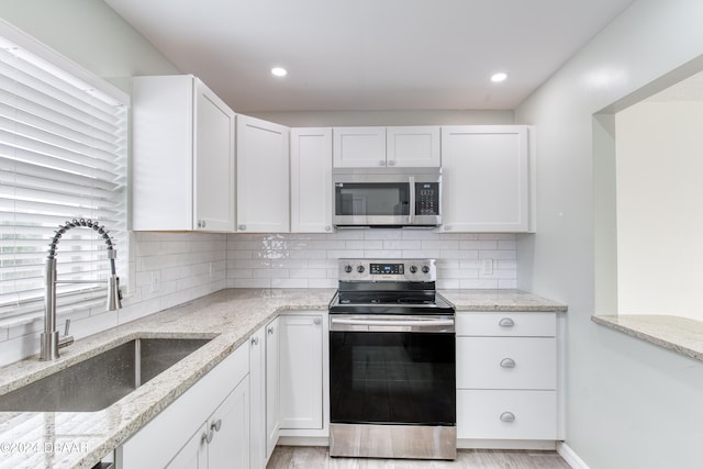 kitchen with light stone counters, sink, white cabinetry, light wood-type flooring, and appliances with stainless steel finishes